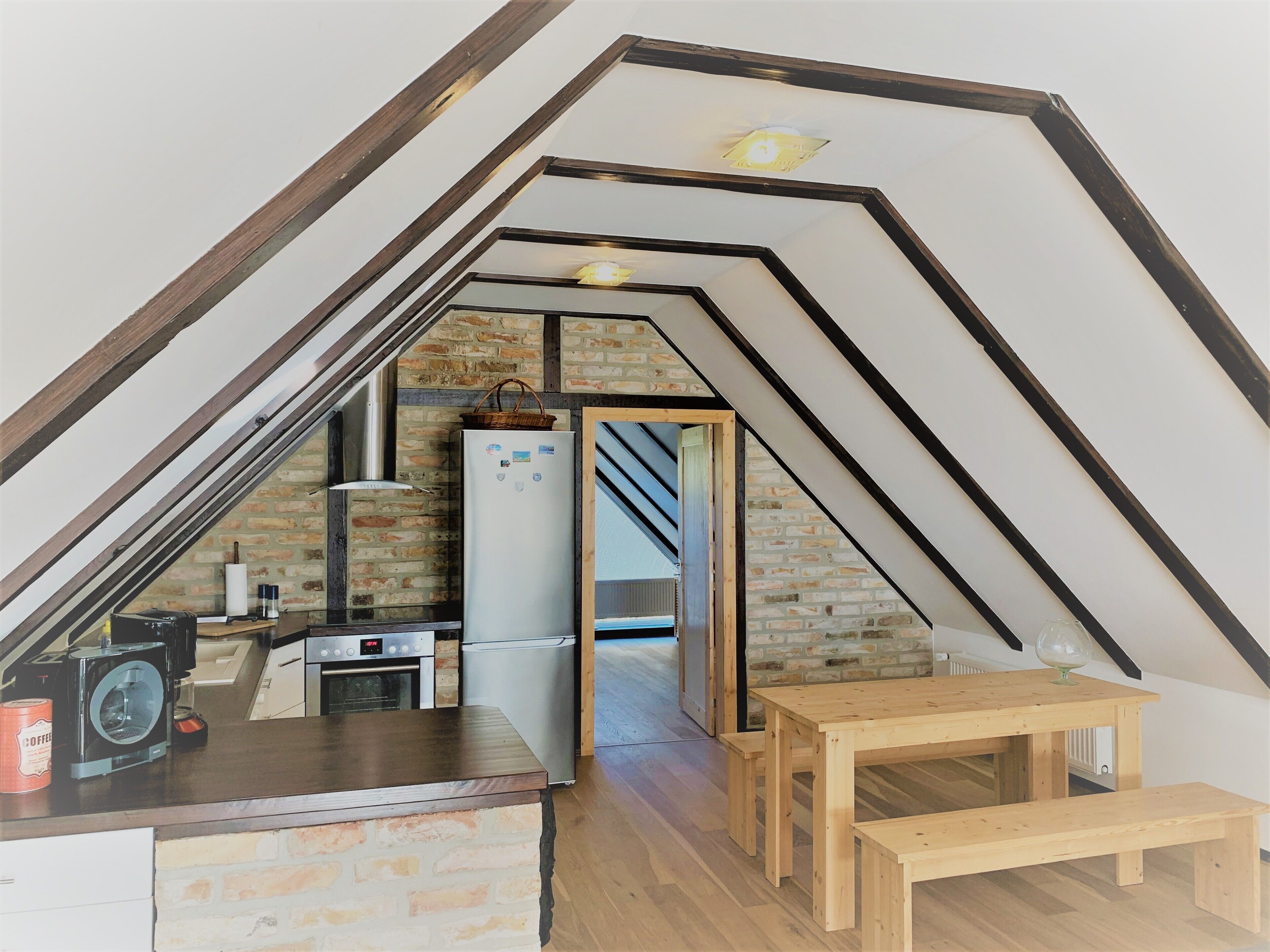 A kitchen with a brick wall, wooden beams, and a wooden table with benches.