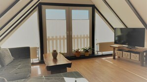 Una habitación acogedora con piso de madera, un sofá, una mesa y un televisor sobre un soporte de madera.
