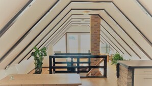 Un dormitorio tipo loft moderno con techo inclinado, una mesa de madera, chimenea de ladrillo y vistas al exterior.