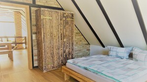 Un dormitorio con techo inclinado, suelo de madera, cama con colcha y un armario.