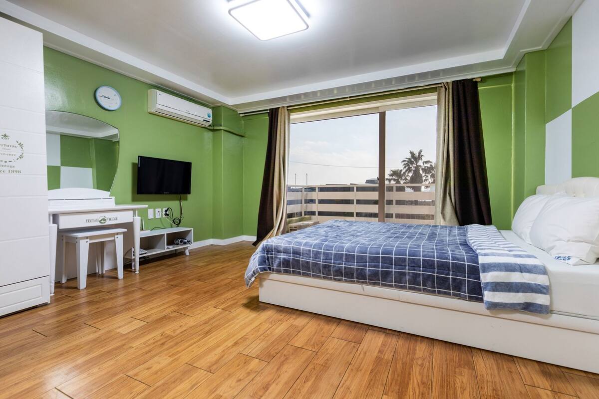 Ein Schlafzimmer mit einem Bett, einem Schreibtisch, einem Stuhl, einem Fernseher und einem Fenster mit Vorhängen.