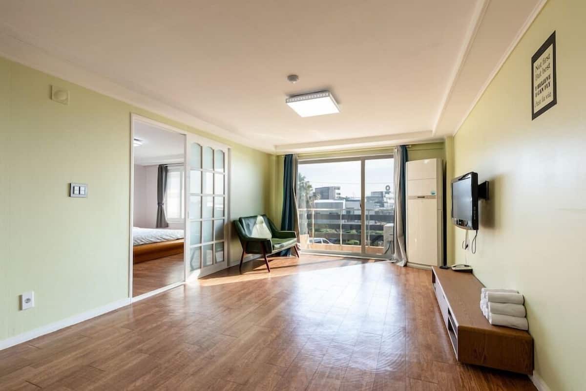 Ein geräumiges Zimmer mit Balkon, einem Bett, einem grünen Sessel, einem Fernseher und einer Bank mit Handtüchern.
