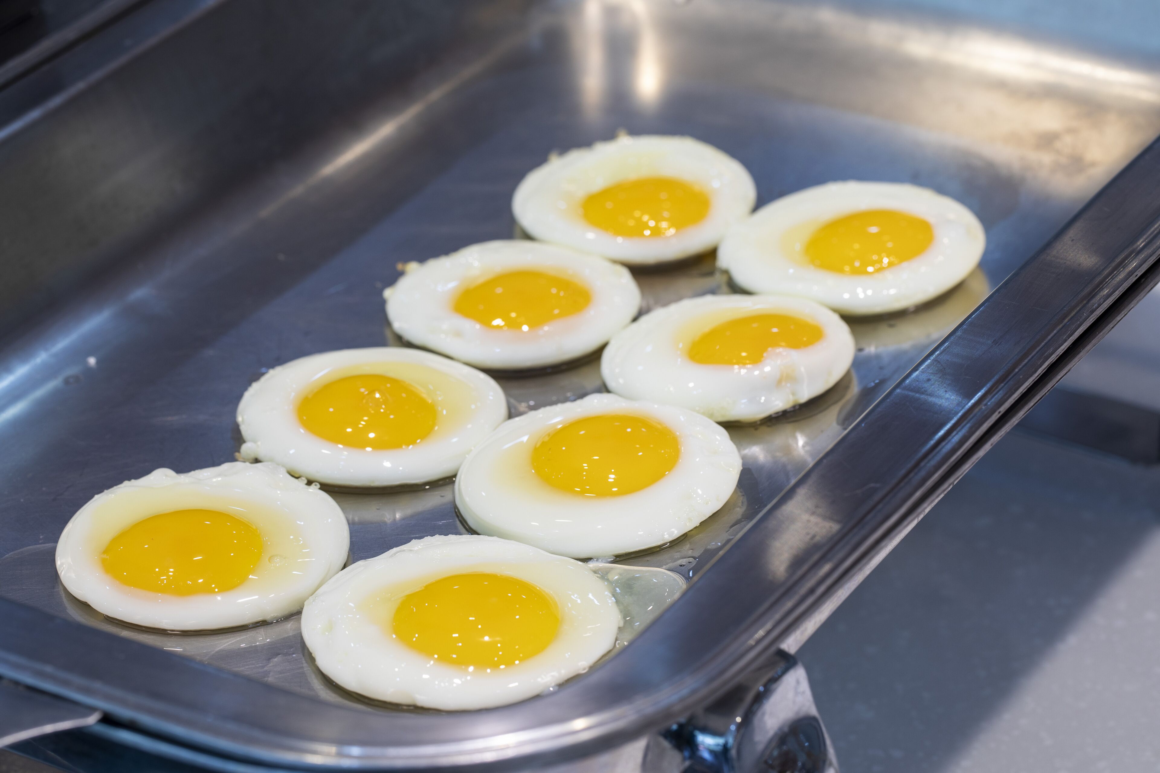 A stainless steel tray with six fried eggs.