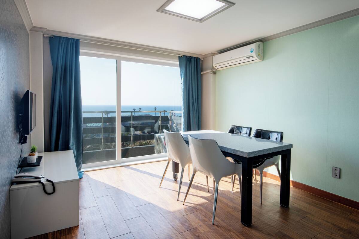 Ein modernes Zimmer mit Esstisch, Stühlen, einem kleinen Schreibtisch und einem großen Fenster mit Blick.