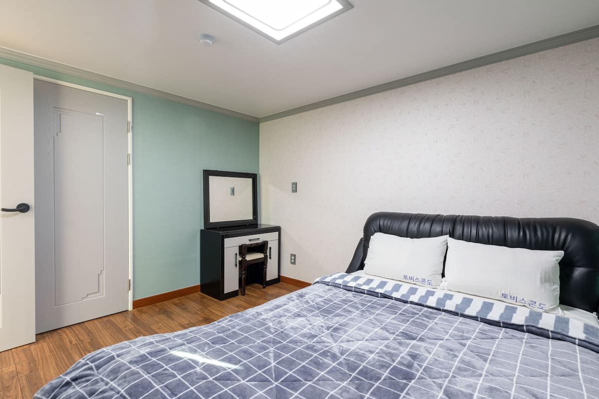 Ein Schlafzimmer mit Bett, Schreibtisch, Stuhl, Tür und Deckenleuchte.