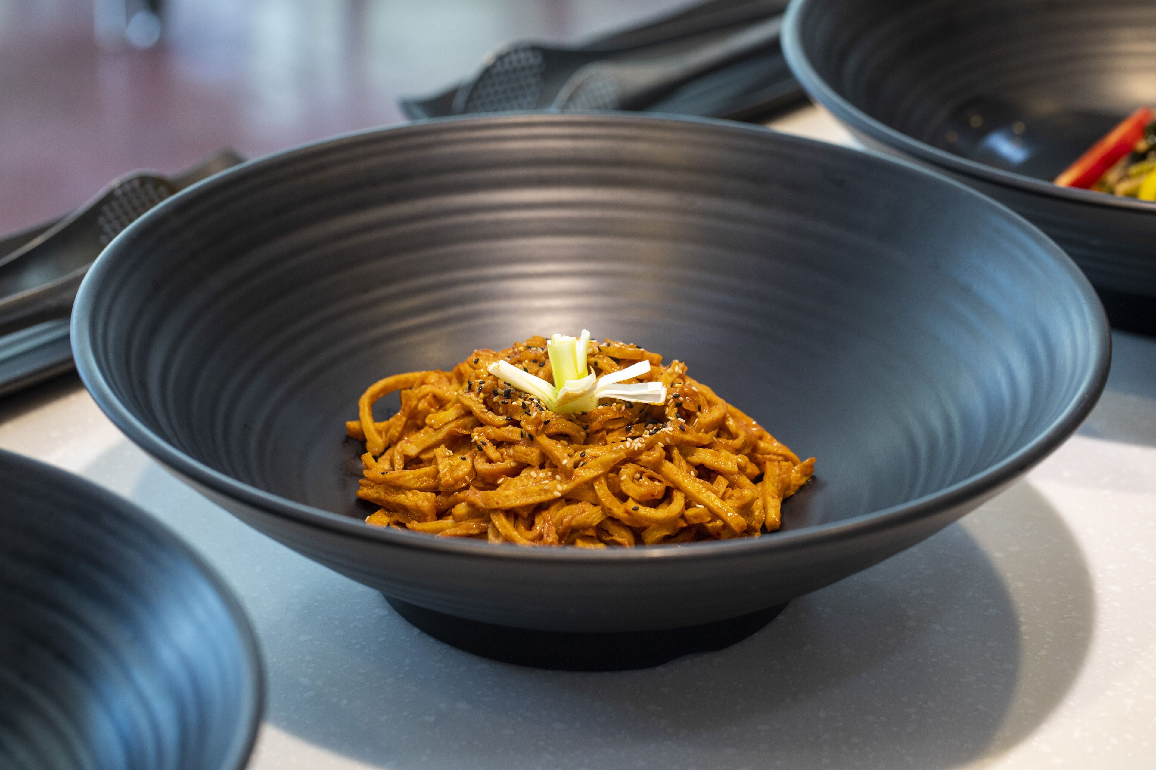 A bowl of noodles garnished with sesame seeds and a slice of ginger.