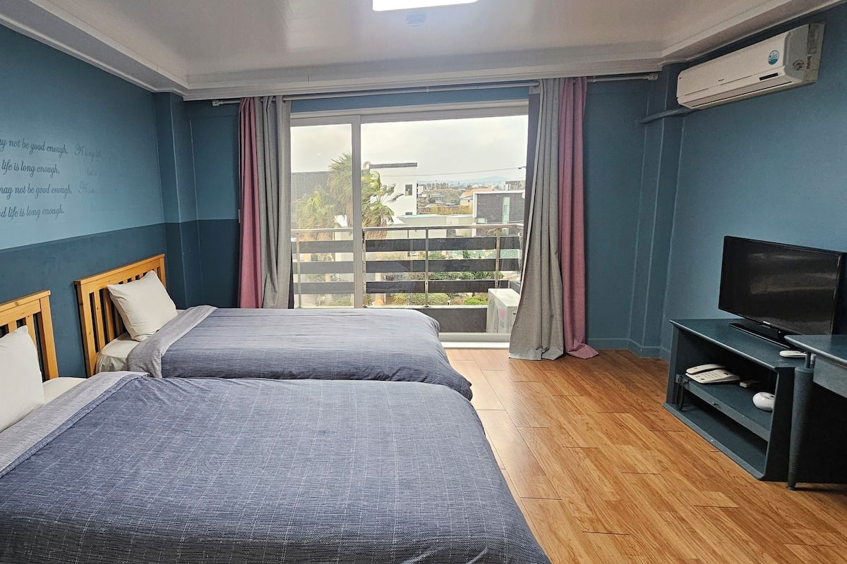 Ein Hotelzimmer mit zwei Betten, einem Fernseher und einem Balkon mit Blick auf Gebäude.