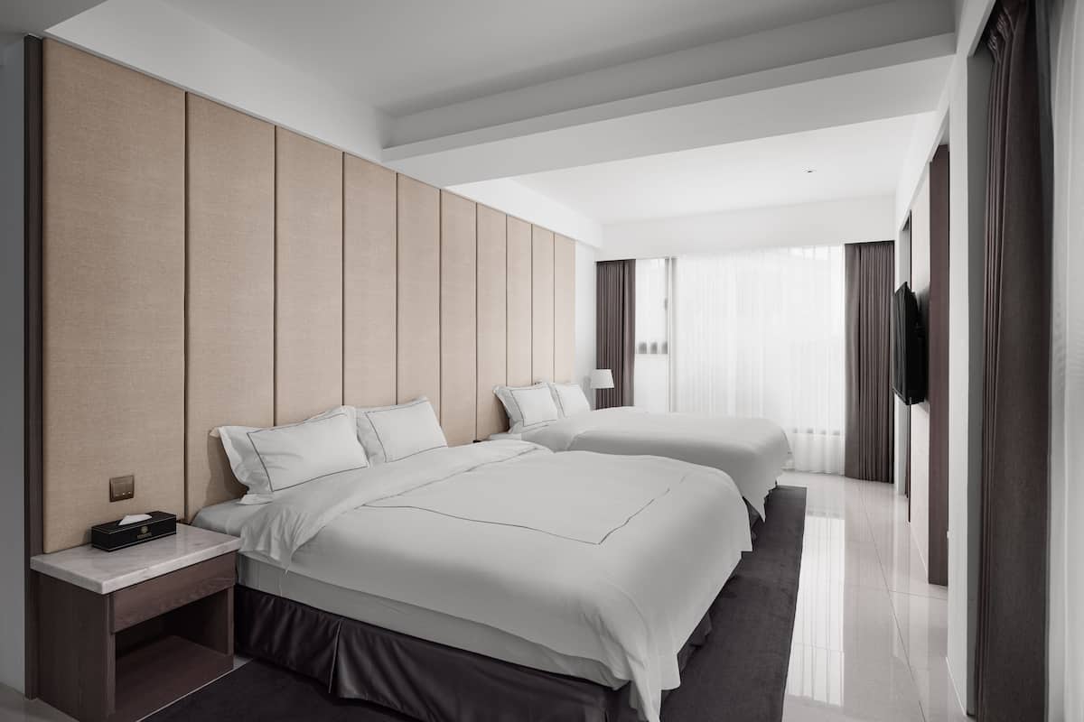 A modern hotel room with two beds, a flat-screen TV, and a large window with curtains.