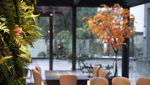 An indoor dining area with tables and chairs, a large window with a view of a body of water, and a decorative plant with orange leaves. - Gamalan Spring Hotel (Jiaoxi)