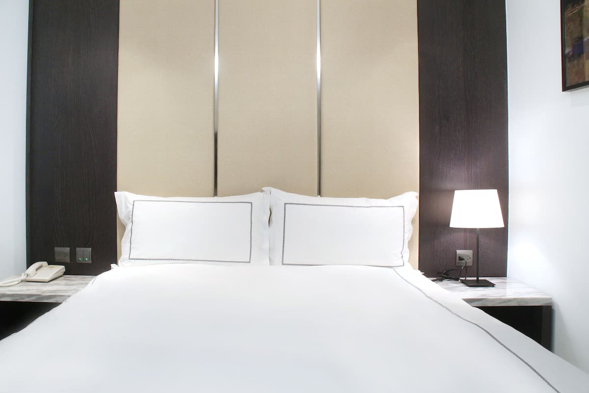 A hotel room with a large bed, two bedside tables, a bedside lamp, and a phone on the left table.