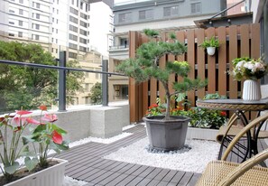 A rooftop terrace with a potted pine tree, white pebbles, wicker furniture, and a wooden fence. - Gamalan Spring Hotel (Jiaoxi)