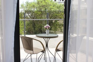 A balcony with wicker chairs and a glass table, a vase with flowers, and a view of trees and a building in the background. - Gamalan Spring Hotel (Jiaoxi)