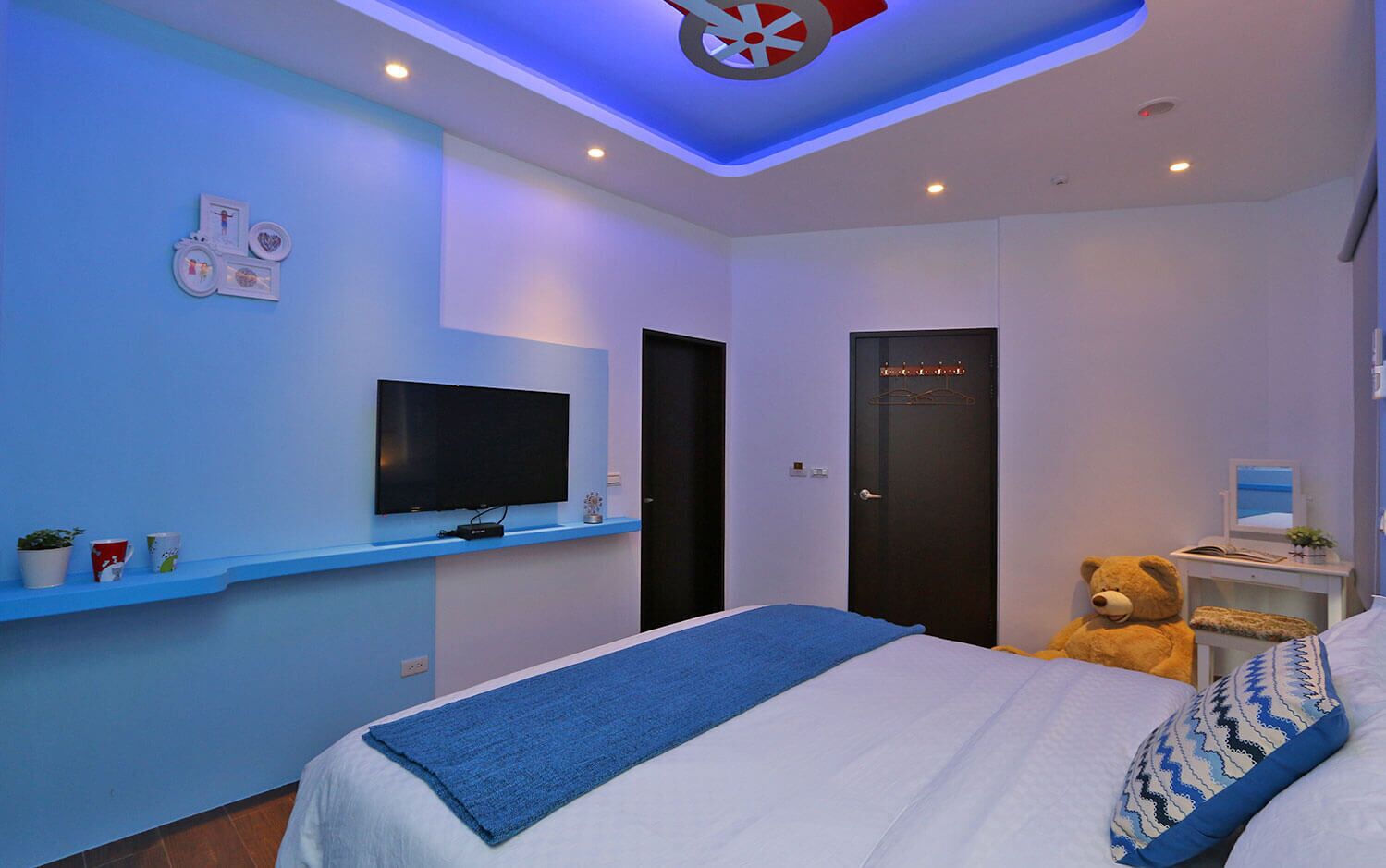 A modern bedroom with a bed, a TV, a teddy bear, and a desk with a computer.