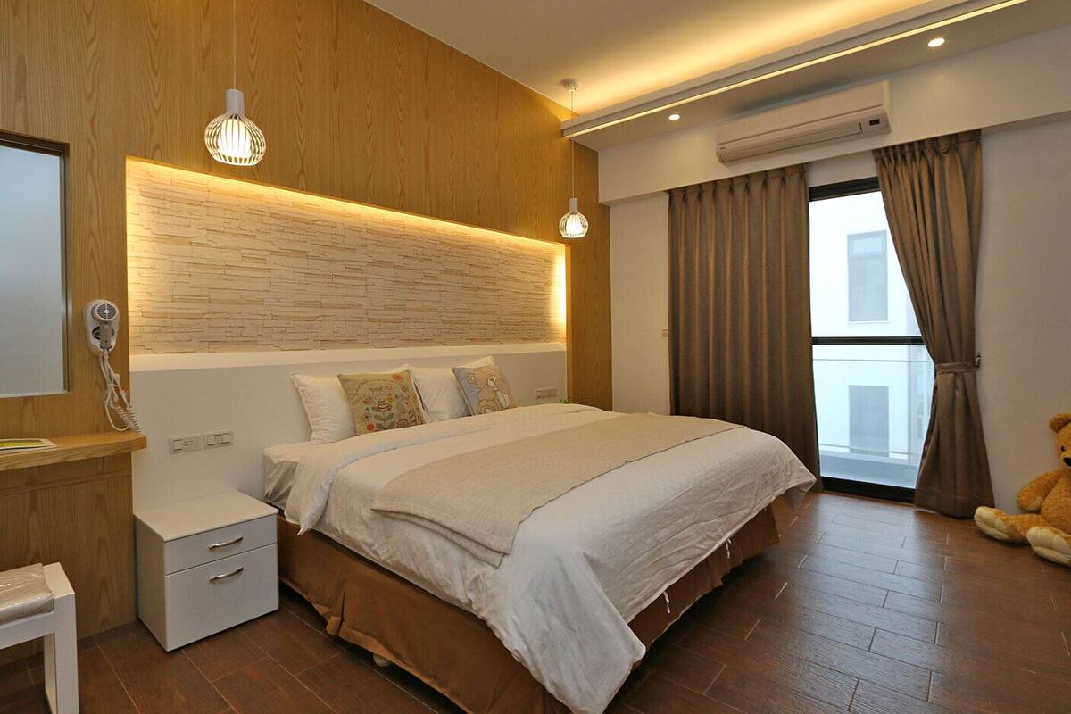 A modern bedroom with a large bed, bedside tables, a wooden headboard, and a teddy bear on the floor.