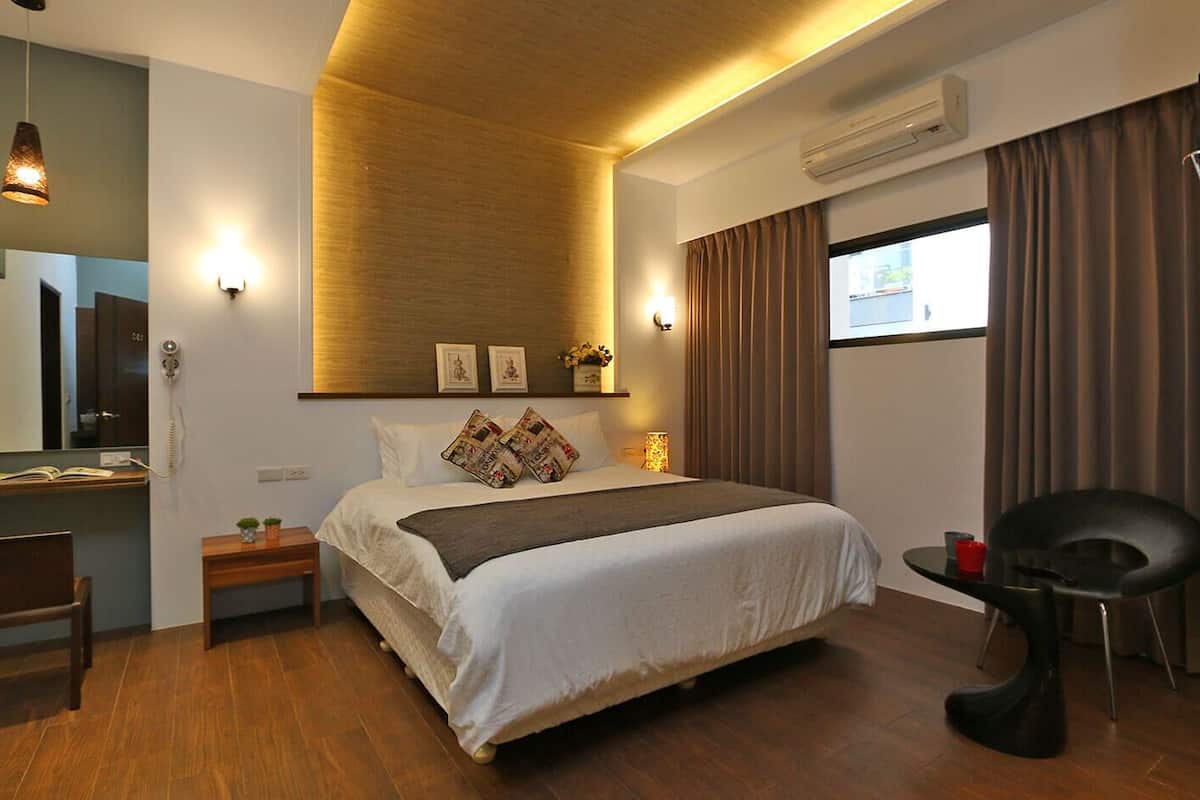 A modern hotel room with a large bed, a desk, a chair, and a window with curtains.