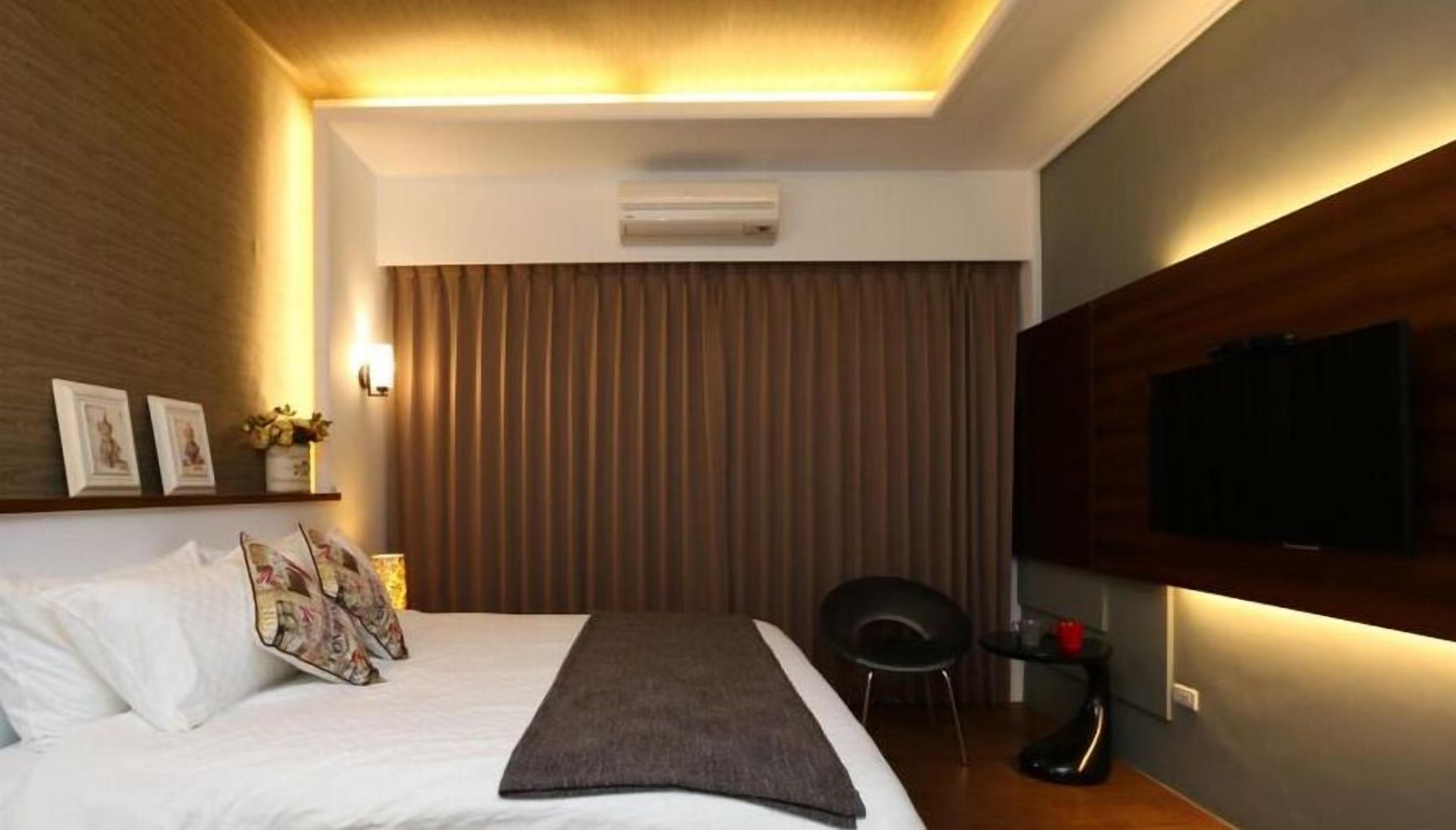 A modern hotel room with a large bed, a flat-screen TV mounted on the wall, and a ceiling air conditioner.