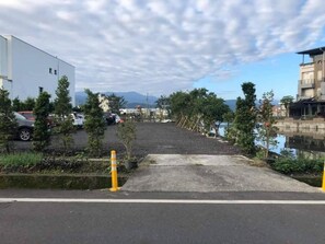 A parking area with a paved walkway leading to a building, surrounded by trees and a body of water. - Qing Xin Ju Homestay (Luodong)