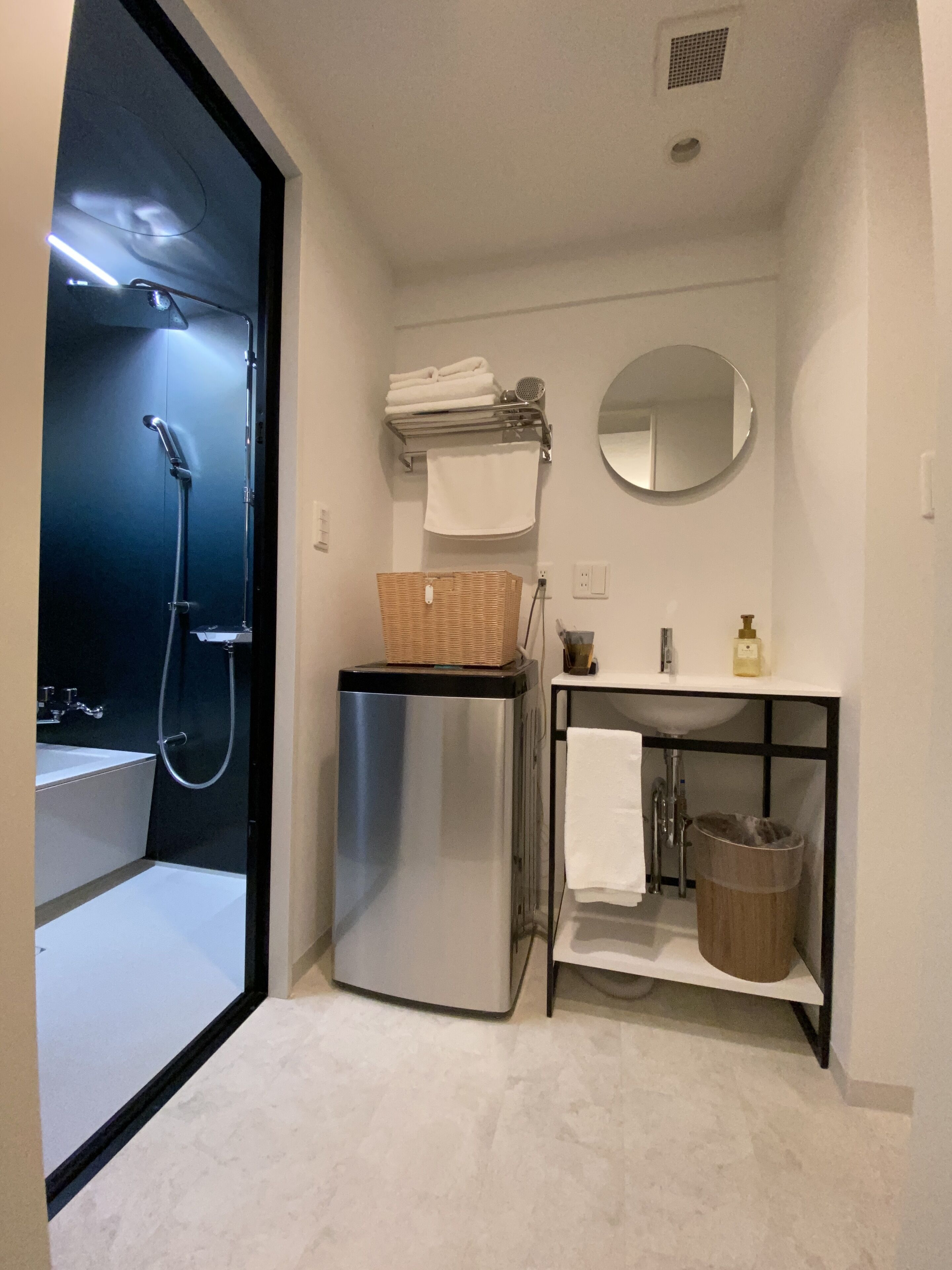 A compact bathroom with a shower, a sink, a mirror, and a small refrigerator.