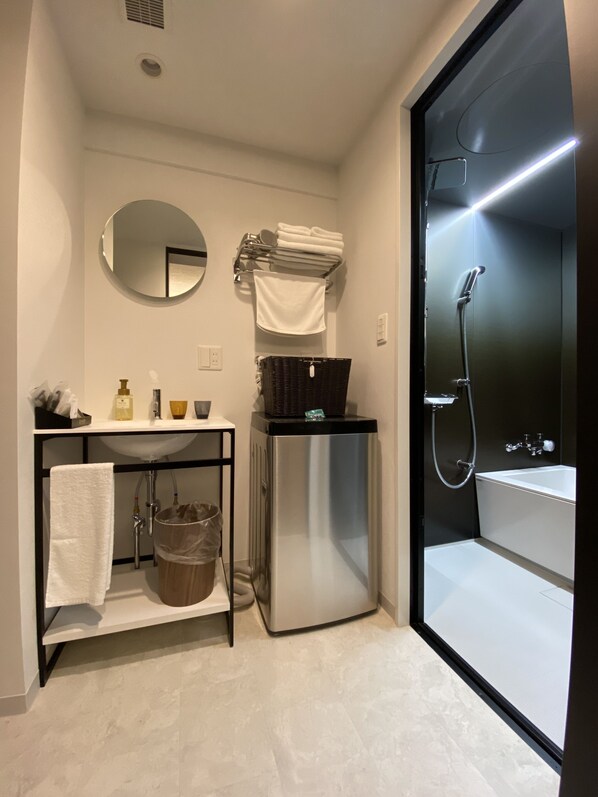 A compact bathroom with a sink, mirror, towel rack, and a shower area.