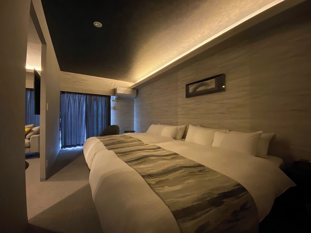 Quarto de hotel moderno com uma cama grande, televisão de tela plana e vista para a cidade.