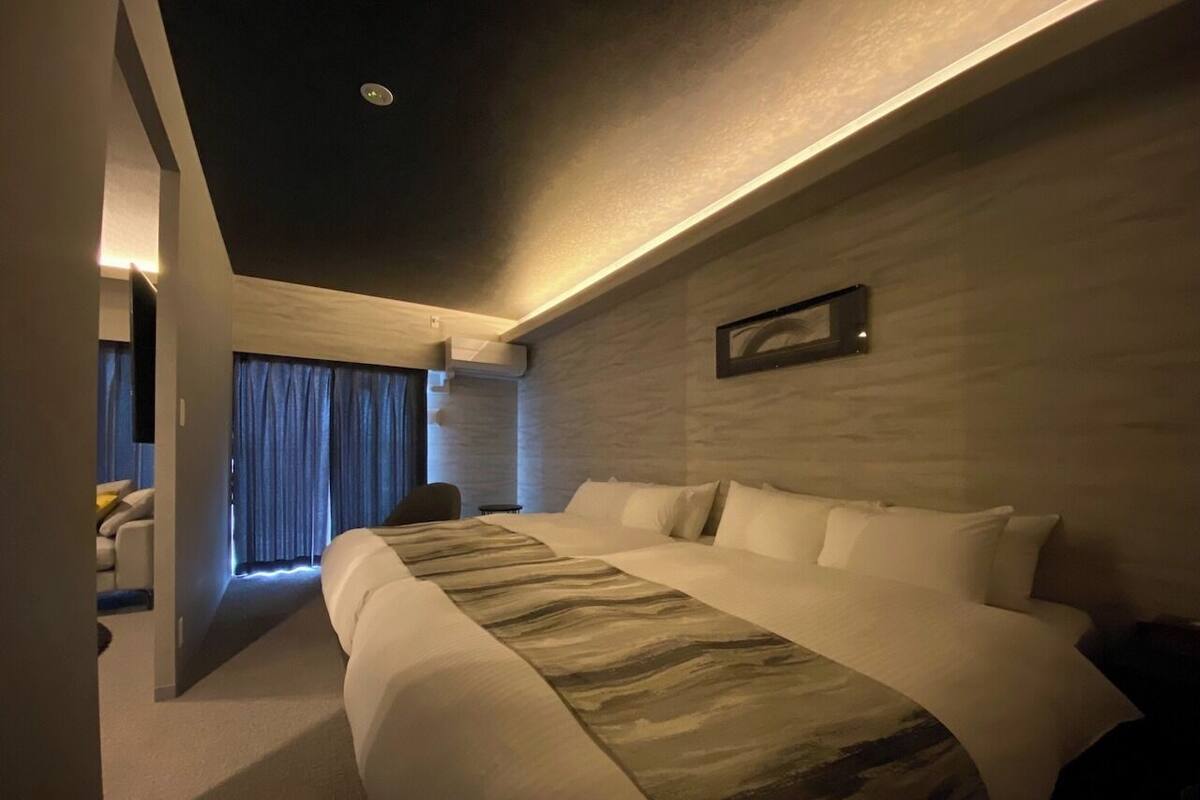 A modern hotel room with a large bed, a flat-screen TV, and a view of the cityscape.