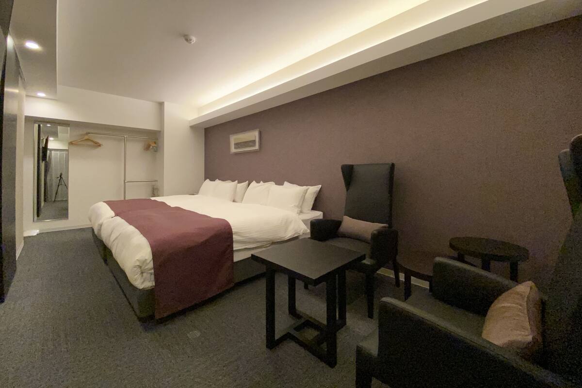A hotel room with a bed, a desk, two chairs, a mirror, and a coat rack.
