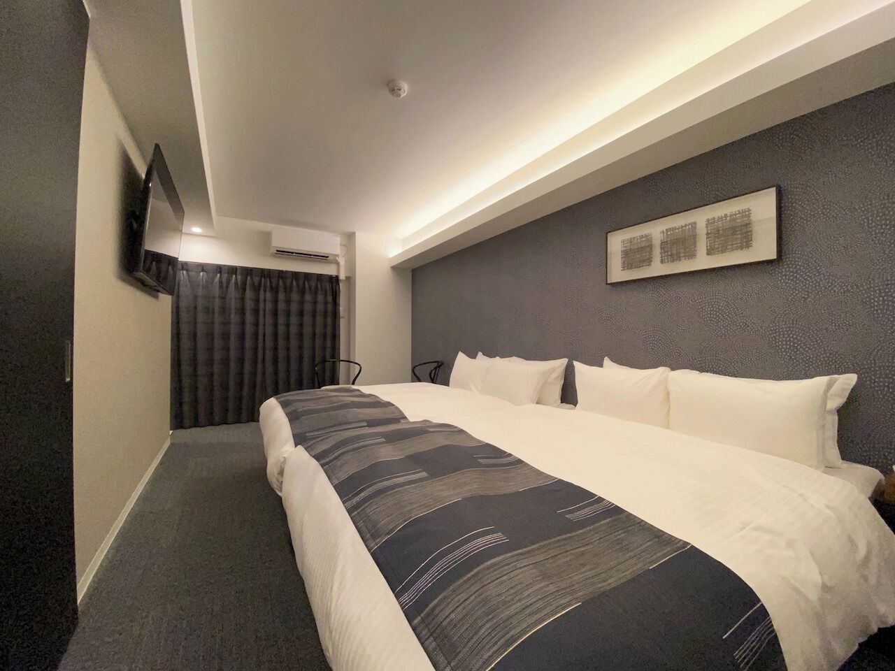 Quarto de hotel com uma cama grande, televisão de tela plana na parede e uma luminária no teto.