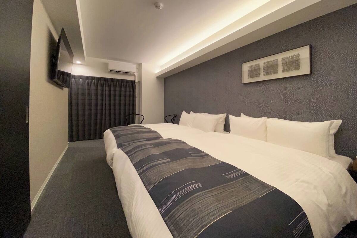 A hotel room with a large bed, a flat-screen TV mounted on the wall, and a ceiling light.