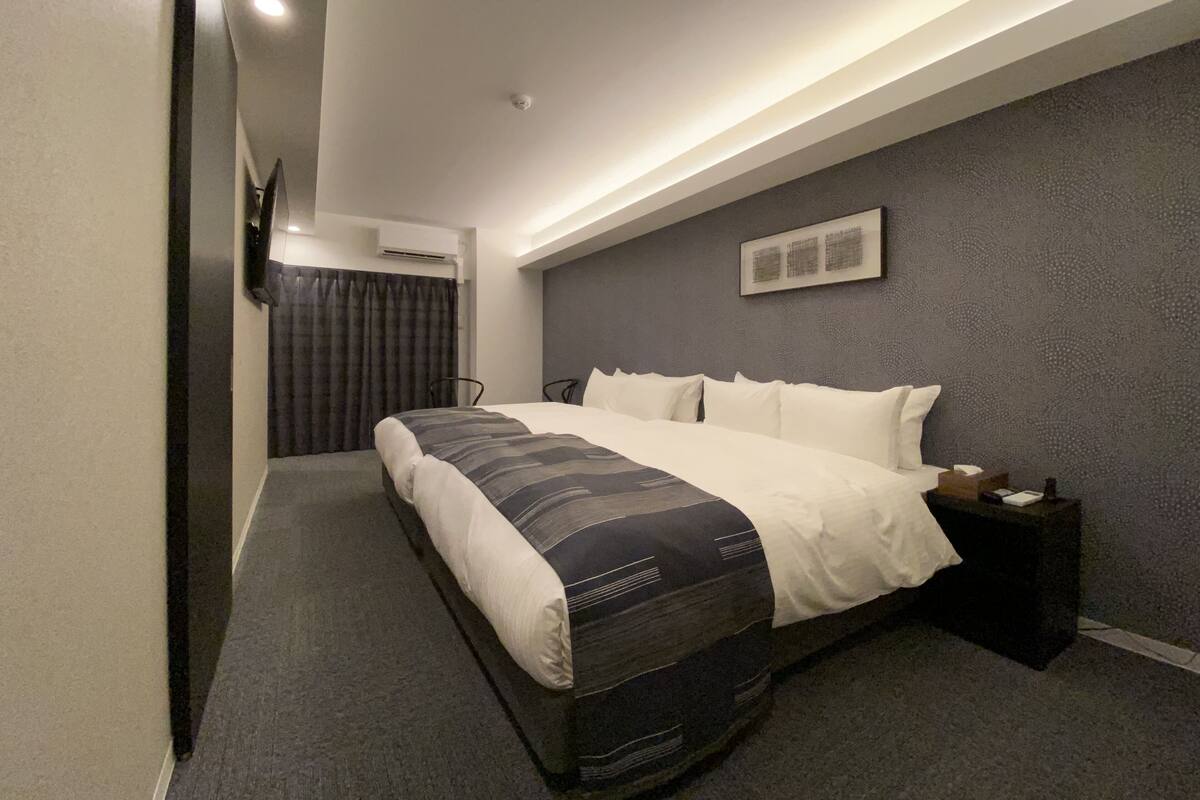A modern hotel room with a large bed, a bedside table, an air conditioning unit, and a framed picture on the wall.
