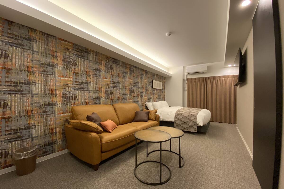 A modern hotel room with a sofa, a bed, a small round table, and a patterned wall.