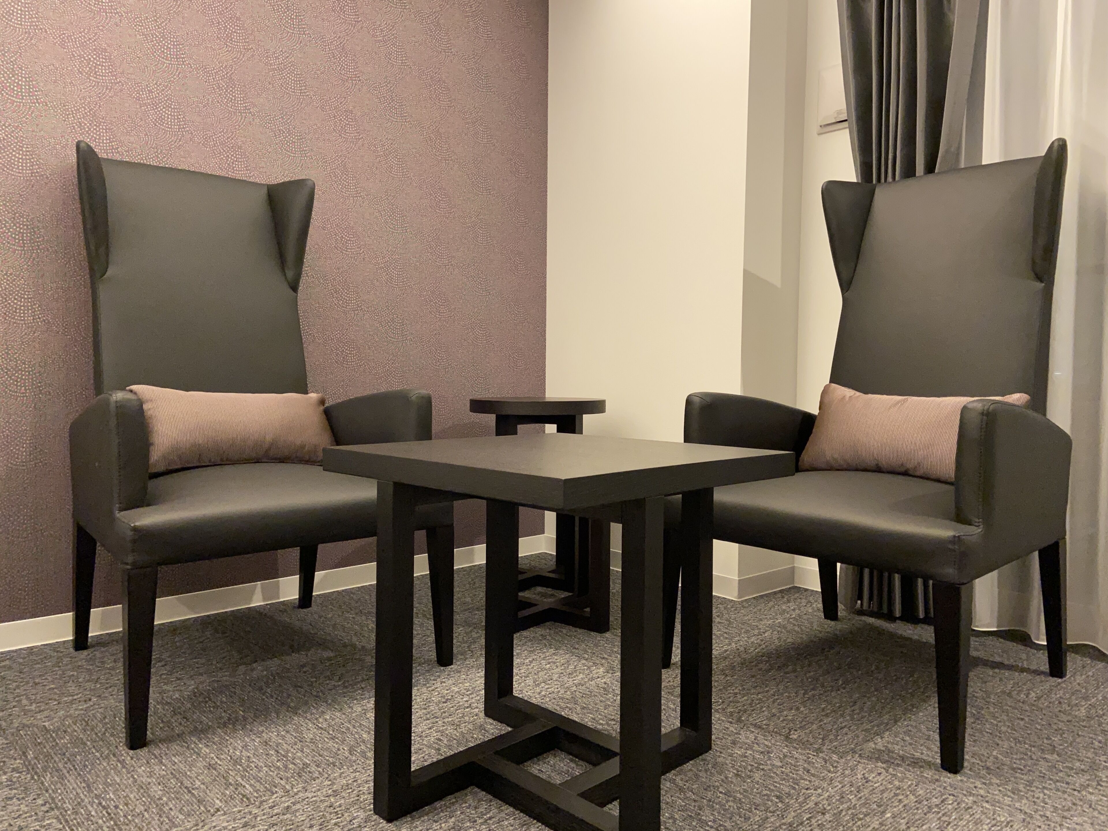 A room with two black leather chairs with cushions, a small table, and a patterned wall.