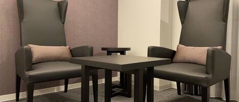 A room with two black leather chairs with cushions, a small table, and a patterned wall.