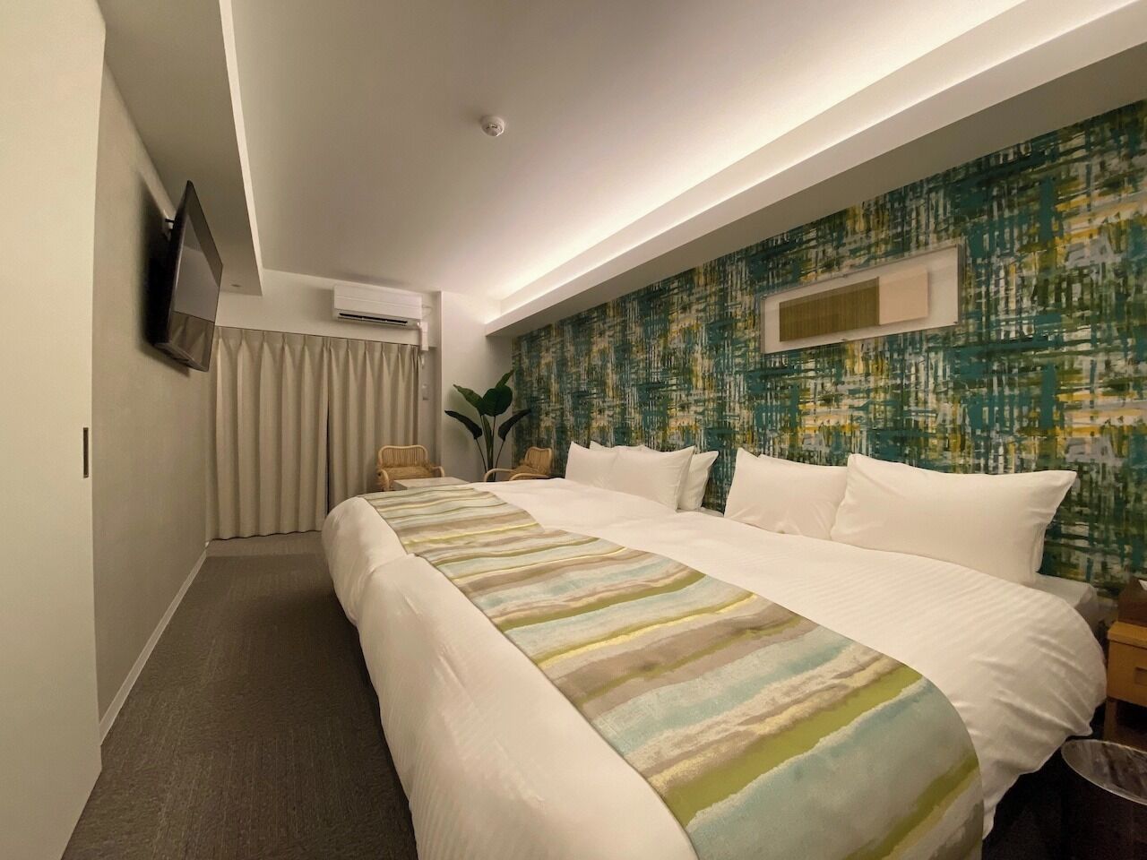 Quarto de hotel com uma cama grande, televisão de tela plana na parede, janela com cortinas e parede com textura.