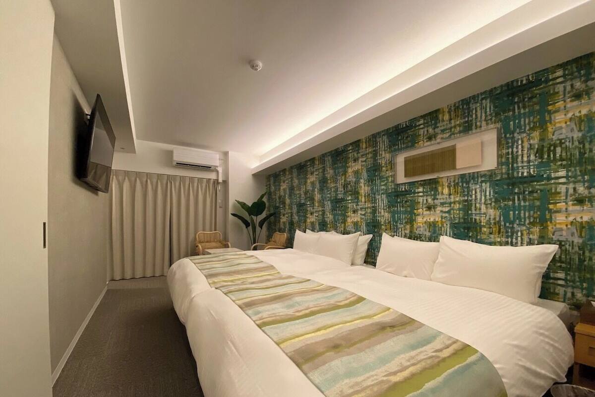 A hotel room with a large bed, a flat-screen TV mounted on the wall, a window with curtains, and a wall with a textured pattern.