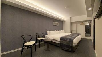 A modern hotel room with a large bed, two chairs, a small table, a mirror, and a picture on the wall.