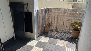 A balcony with a checkered floor, a black grill, and two potted plants. - Charming 2-room apartment, city center, loggia, parking (Sète)