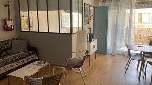 A living room with a sofa, two chairs, a dining table, and a kitchen area with a refrigerator and a coffee machine. - Charming 2-room apartment, city center, loggia, parking (Sète)