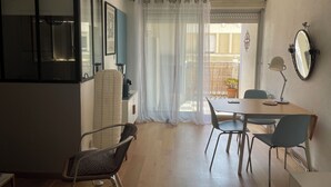 A dining area with a table, chairs, and a kitchen area with a refrigerator and a blender. - Charming 2-room apartment, city center, loggia, parking (Sète)