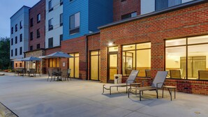 A building with a brick facade and large windows, outdoor seating area with chairs and umbrellas, and a paved patio. - Fairfield Inn & Suites by Marriott Asheville Weaverville (Weaverville)
