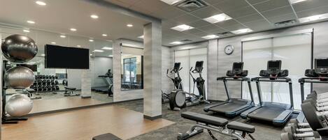 A modern gym with exercise equipment, a large mirror, and a television.