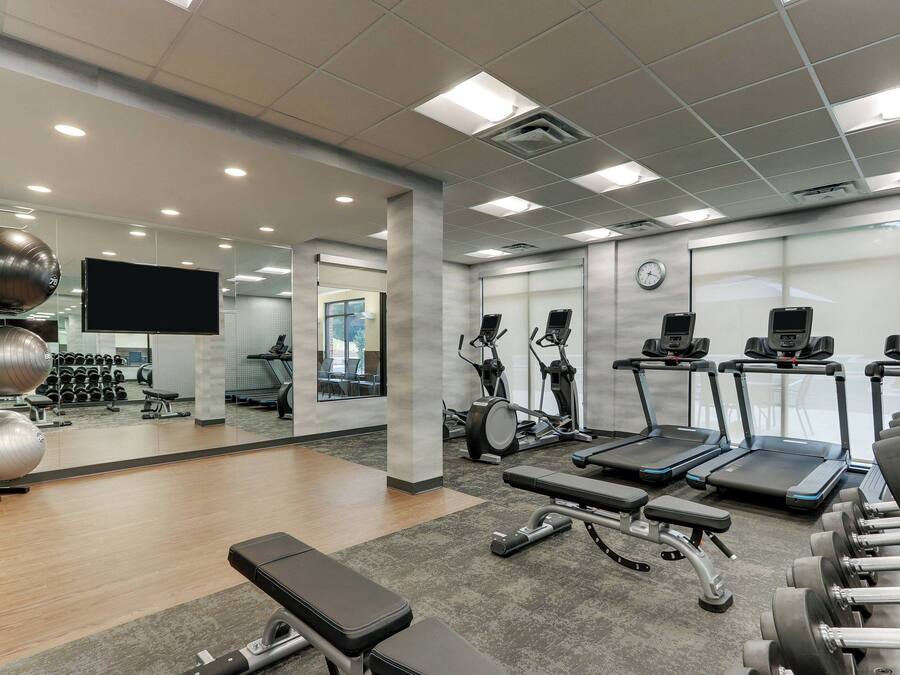 Un gimnasio moderno con equipo de ejercicio, un espejo grande y una televisión.