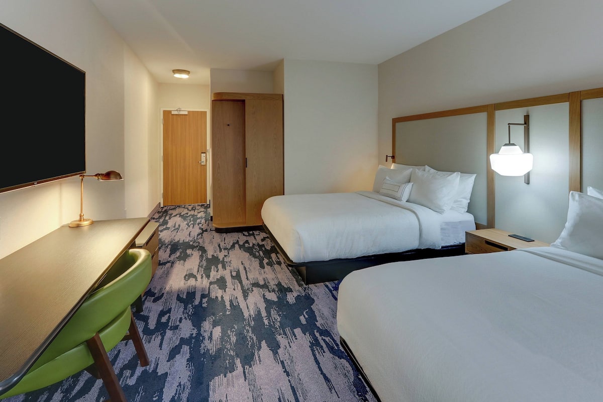A hotel room with two beds, a desk, a chair, and a TV.