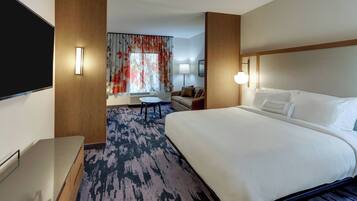 A hotel room with a large bed, a desk, a chair, a sofa, and a TV.