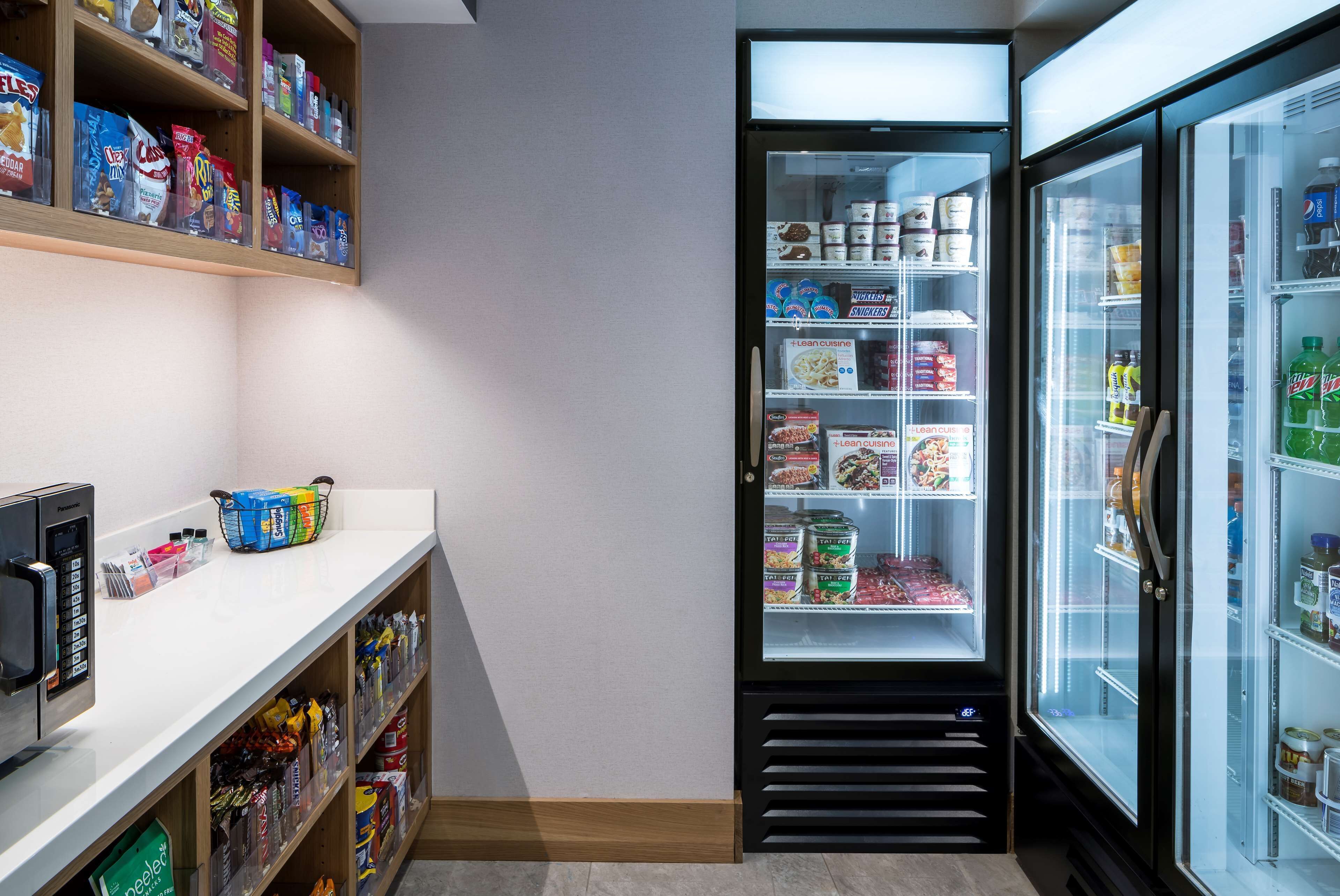Una cuina compacta equipada amb microones, un refrigerador ple d'aliments i una estant amb aperitius.