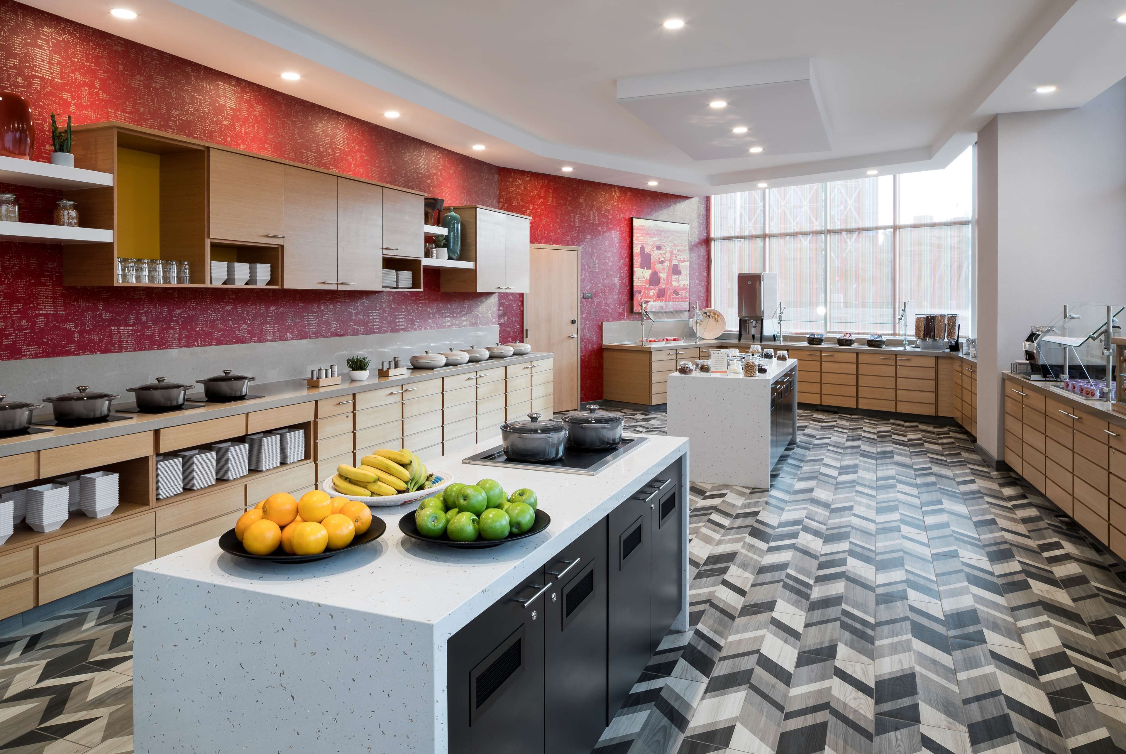 Una cocina moderna con una isla central, armarios de madera y una pared roja con textura.