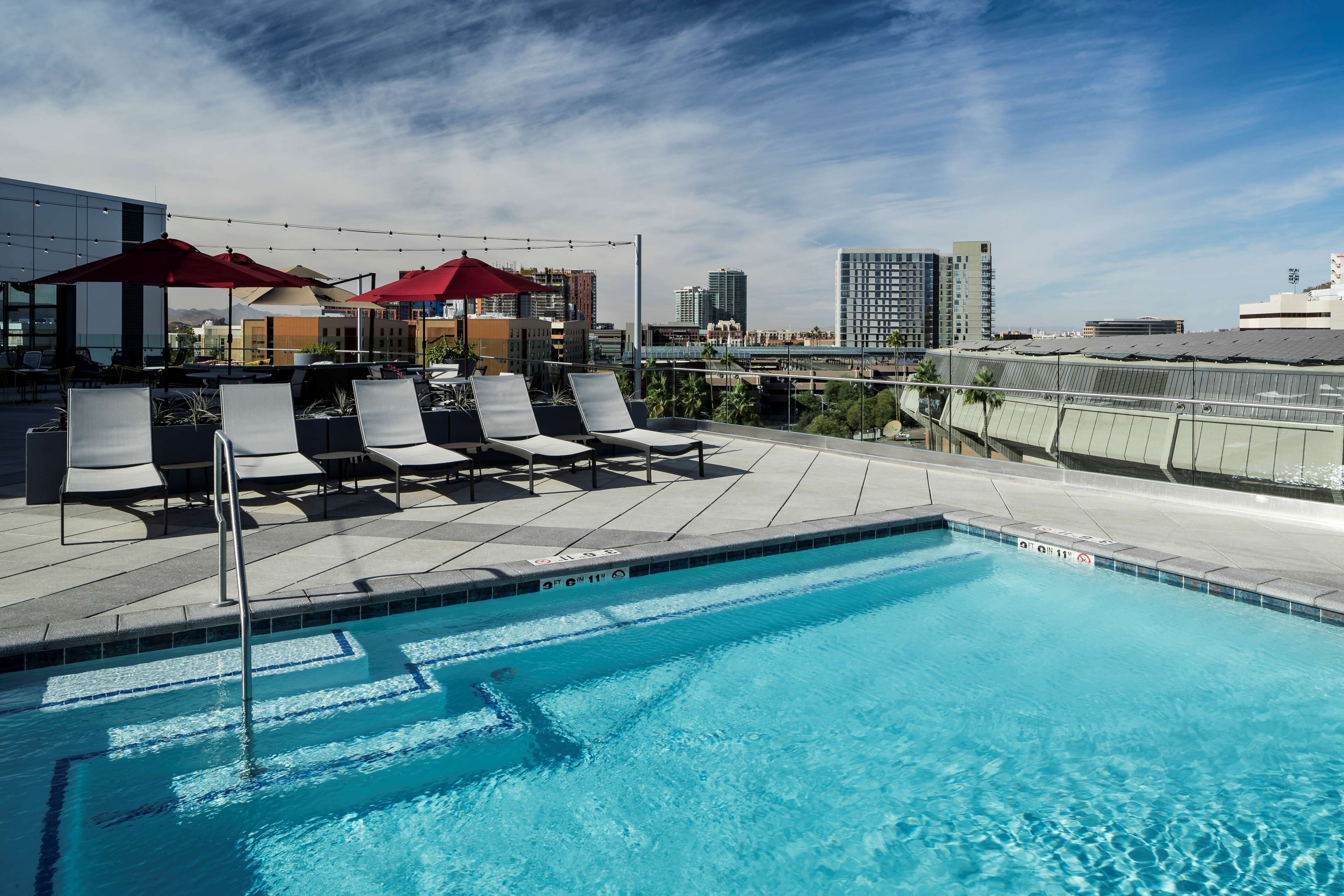 A rooftop pool with lounge chairs and umbrellas, surrounded by city buildings.