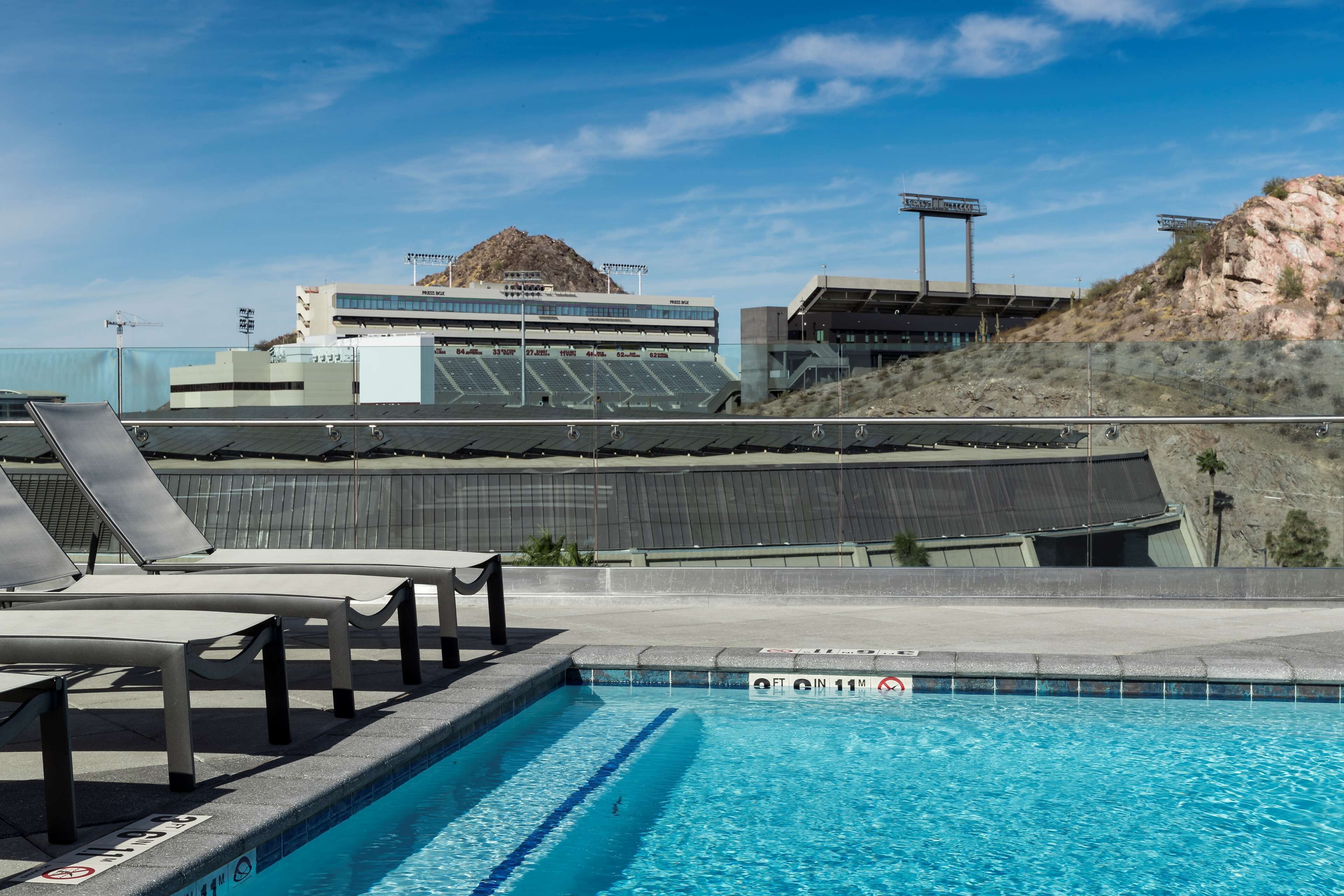 A swimming pool with lounge chairs and a view of a building with a large rock formation in the background.