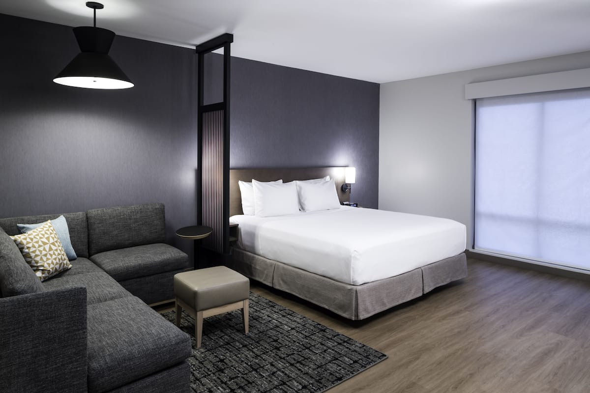 Moderni hotellihuone, jossa on suuri sänky, sohva, pieni pöytä ja suuri ikkuna.