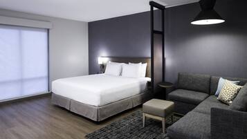 Una moderna camera d'albergo con un letto grande, un divano grigio, un tavolino e un'ampia finestra con tende.