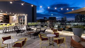 Un bar situé sur un toit, avec une terrasse, une vue sur la ville et des guirlandes lumineuses.